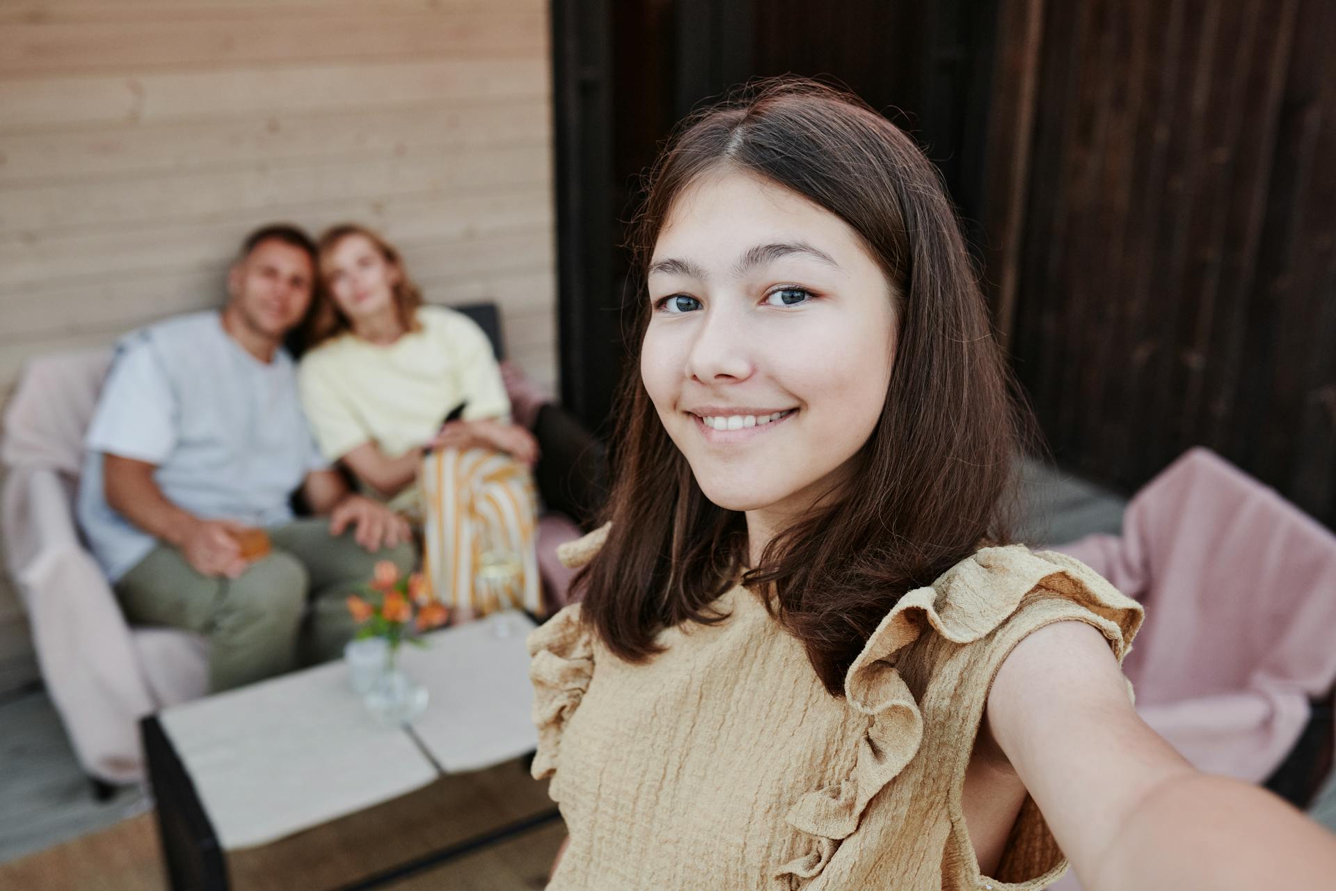 Ein Teenager-Mädchen macht ein Selfie mit zwei Erwachsenen im Hintergrund | Quelle: Pexels