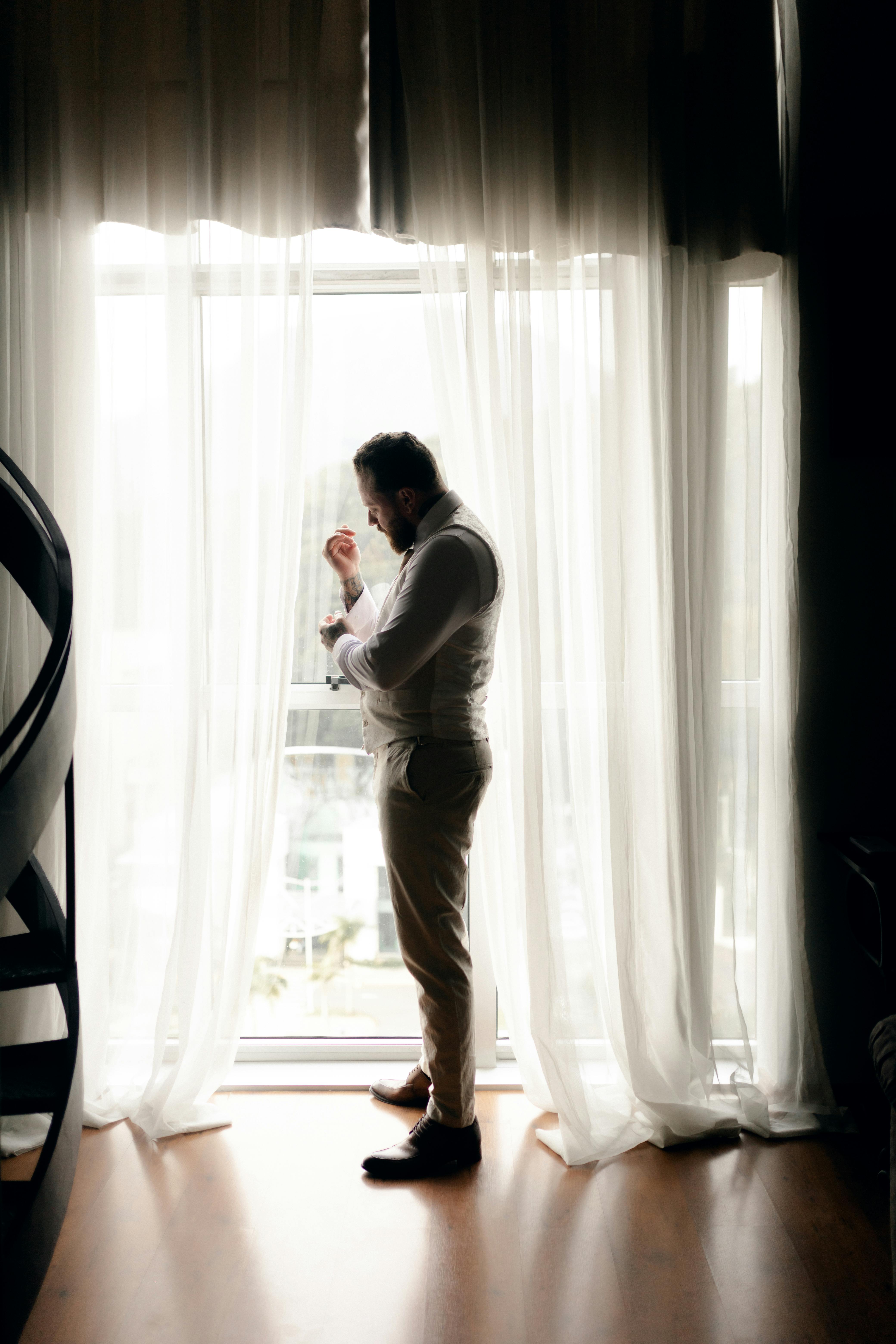 Mann steht am Fenster und passt seinen Anzug an | Quelle: Pexels
