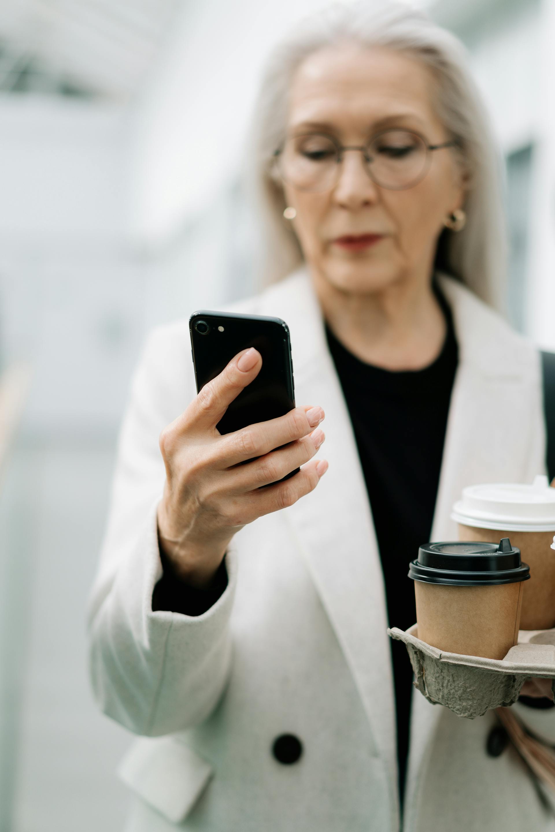 Eine ältere Frau, die ihr Telefon benutzt, während sie einen Kaffee in der Hand hält | Quelle: Pexels