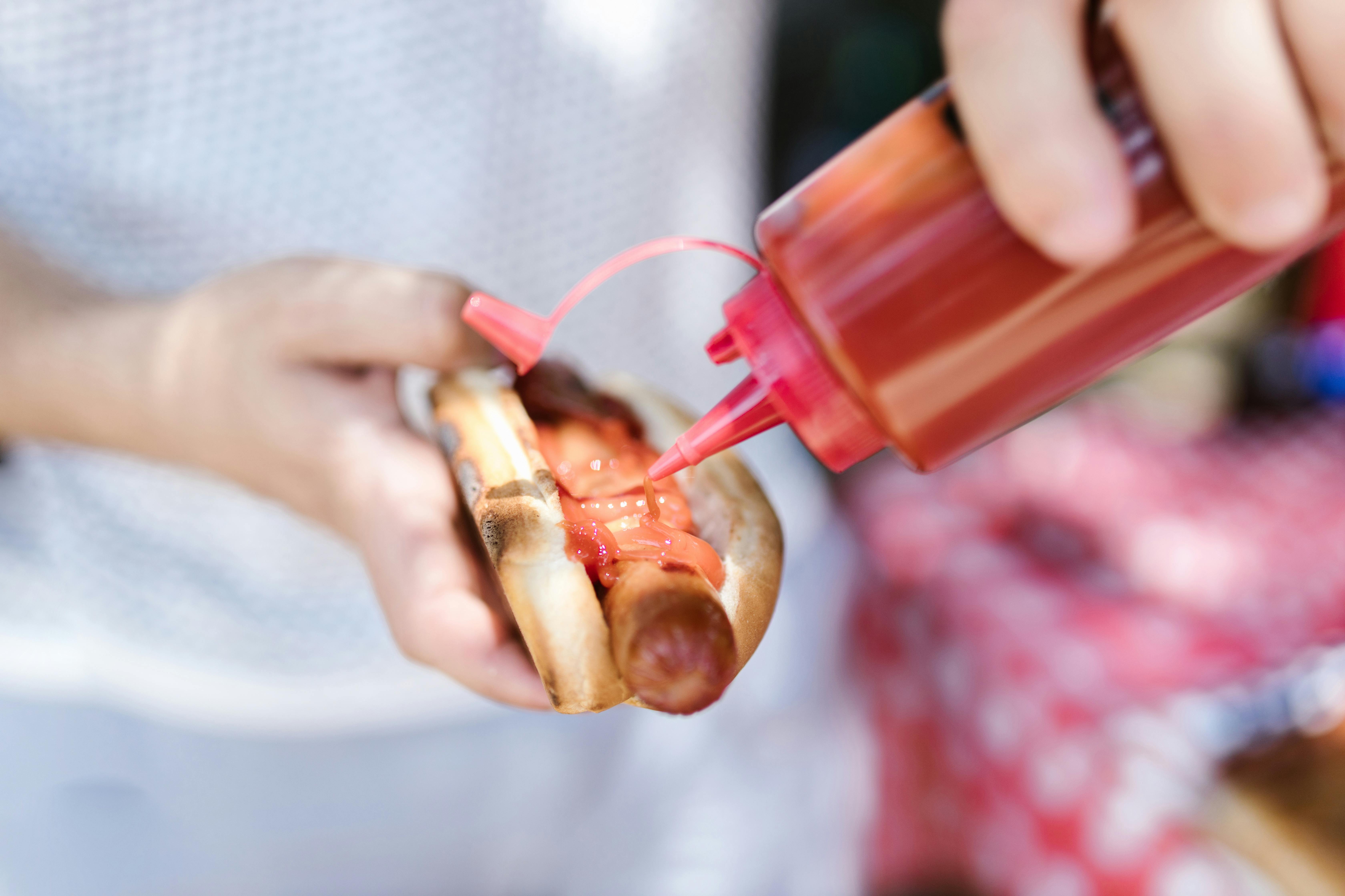 Eine Person, die Ketchup auf einen Hotdog schmiert | Quelle: Pexels
